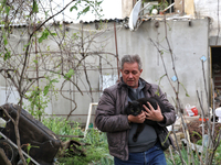 A man is carrying a black cat across a yard in a residential area affected by falling Russian missile debris in the Odesa region, southern U...