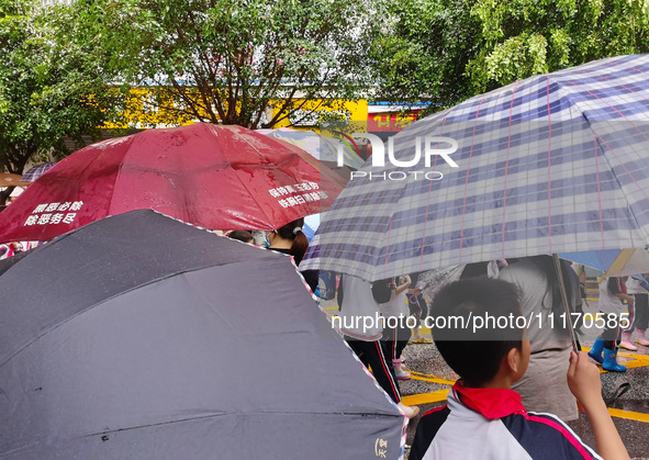 Parents are holding umbrellas to pick up students at the school gate as kindergarten classes resume at noon in Qingyuan, China, on April 23,...