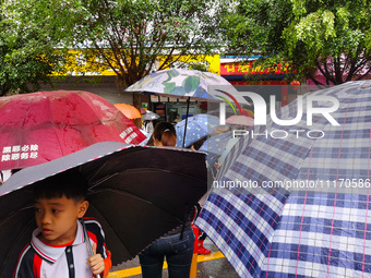 Parents are holding umbrellas to pick up students at the school gate as kindergarten classes resume at noon in Qingyuan, China, on April 23,...