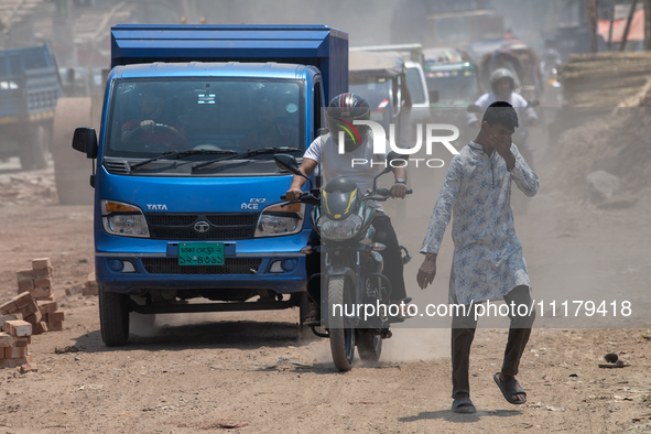 People are walking along a dusty, busy road in Dhaka, Bangladesh, on April 26, 2024. 