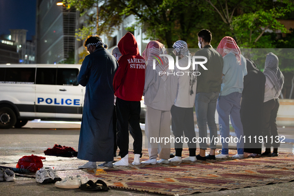 Muslim students pray at sunrise at a Gaza solidarity encampment at George Washington University, while a DC police van blocks the street, Wa...