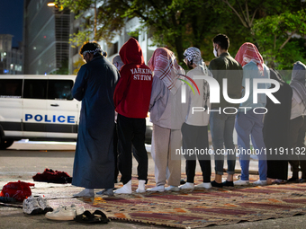 Muslim students pray at sunrise at a Gaza solidarity encampment at George Washington University, while a DC police van blocks the street, Wa...