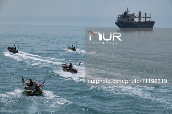 Basij paramilitary force speed boats are sailing along the Persian Gulf near a general cargo vessel during the IRGC marine parade, which is...