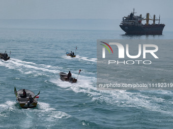 Basij paramilitary force speed boats are sailing along the Persian Gulf near a general cargo vessel during the IRGC marine parade, which is...