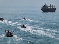 Basij paramilitary force speed boats are sailing along the Persian Gulf near a general cargo vessel during the IRGC marine parade, which is...