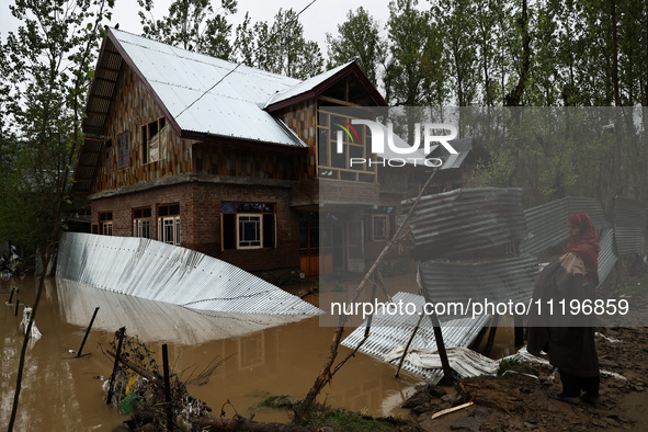 A woman is looking towards her house, which has been submerged, and she had to evacuate due to flash floods on the outskirts of Sopore, Dist...