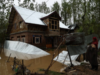 A woman is looking towards her house, which has been submerged, and she had to evacuate due to flash floods on the outskirts of Sopore, Dist...