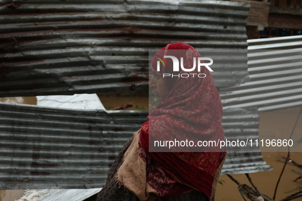 A woman is looking towards her house, which has been submerged, and she had to evacuate due to flash floods on the outskirts of Sopore, Dist...