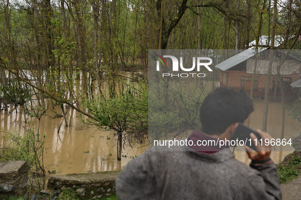 A man is speaking on his phone while standing near structures that are submerged due to flash floods on the outskirts of Sopore, District Ba...