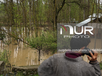 A man is speaking on his phone while standing near structures that are submerged due to flash floods on the outskirts of Sopore, District Ba...