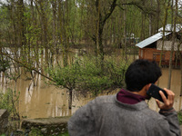 A man is speaking on his phone while standing near structures that are submerged due to flash floods on the outskirts of Sopore, District Ba...