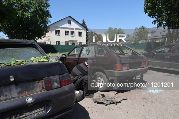 A man is crouching down by the rear wheel of a car that has been damaged by a Russian strike in Zolochiv, Ukraine, on May 1, 2024, with guid...