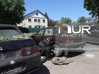 A man is crouching down by the rear wheel of a car that has been damaged by a Russian strike in Zolochiv, Ukraine, on May 1, 2024, with guid...