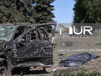 A human remains pouch containing the body of a victim is lying on the ground next to a damaged car after a Russian strike in Zolochiv, Khark...