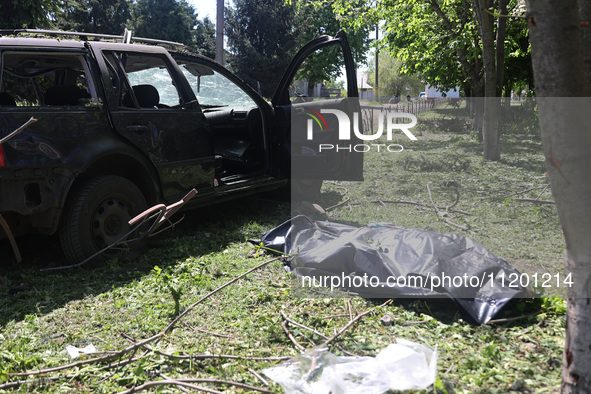 A human remains pouch containing the body of a victim is lying on the ground next to a damaged car after a Russian strike in Zolochiv, Khark...