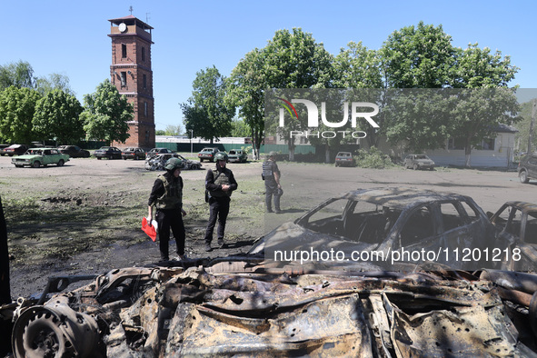 Officials in helmets and ballistic vests are standing by cars destroyed by a Russian strike in Zolochiv, Ukraine, on May 1, 2024. The cars w...