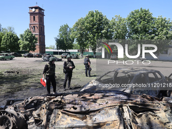 Officials in helmets and ballistic vests are standing by cars destroyed by a Russian strike in Zolochiv, Ukraine, on May 1, 2024. The cars w...