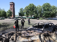 Officials in helmets and ballistic vests are standing by cars destroyed by a Russian strike in Zolochiv, Ukraine, on May 1, 2024. The cars w...