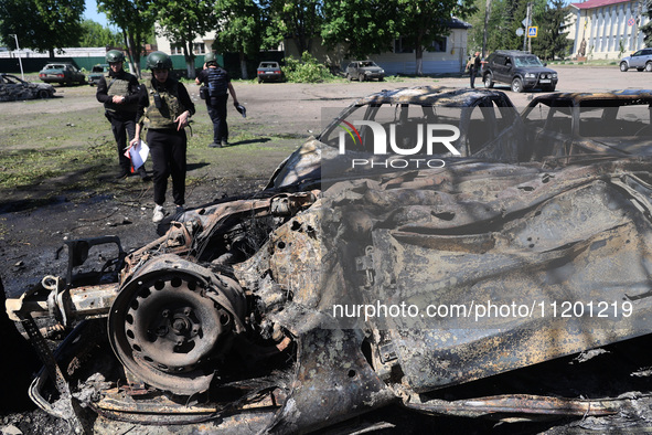 Officials in helmets and ballistic vests are standing by cars destroyed by a Russian strike in Zolochiv, Ukraine, on May 1, 2024. The cars w...