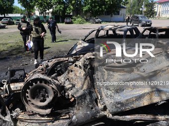 Officials in helmets and ballistic vests are standing by cars destroyed by a Russian strike in Zolochiv, Ukraine, on May 1, 2024. The cars w...