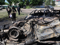 Officials in helmets and ballistic vests are standing by cars destroyed by a Russian strike in Zolochiv, Ukraine, on May 1, 2024. The cars w...