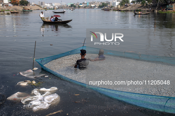 Laborers are cleaning plastic chips on the bank of the Buriganga River while passengers are crossing the river by boat in Dhaka, Bangladesh,...