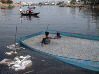 Laborers are cleaning plastic chips on the bank of the Buriganga River while passengers are crossing the river by boat in Dhaka, Bangladesh,...