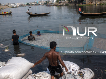 Laborers are cleaning plastic chips on the bank of the Buriganga River while passengers are crossing the river by boat in Dhaka, Bangladesh,...