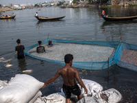 Laborers are cleaning plastic chips on the bank of the Buriganga River while passengers are crossing the river by boat in Dhaka, Bangladesh,...