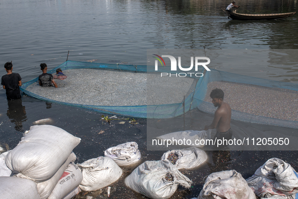 Laborers are cleaning plastic chips on the bank of the Buriganga River while passengers are crossing the river by boat in Dhaka, Bangladesh,...