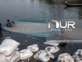 Laborers are cleaning plastic chips on the bank of the Buriganga River while passengers are crossing the river by boat in Dhaka, Bangladesh,...