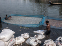 Laborers are cleaning plastic chips on the bank of the Buriganga River while passengers are crossing the river by boat in Dhaka, Bangladesh,...