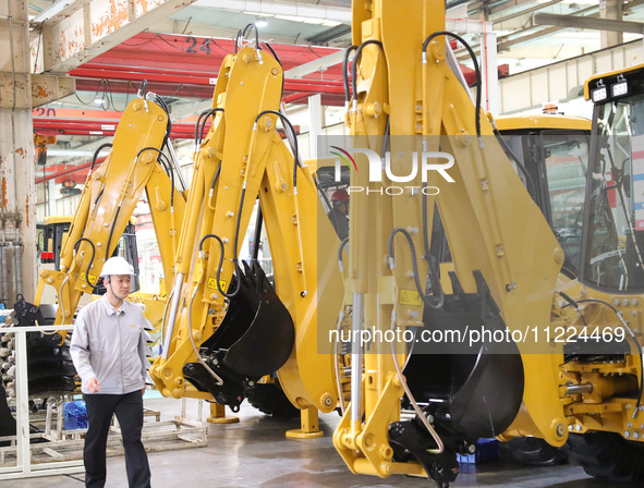 A manager is walking in front of an excavator at the production line of LOVOL Co in Qingdao, Shandong Province, China, on May 9, 2024. 