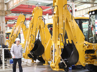 A manager is walking in front of an excavator at the production line of LOVOL Co in Qingdao, Shandong Province, China, on May 9, 2024. (