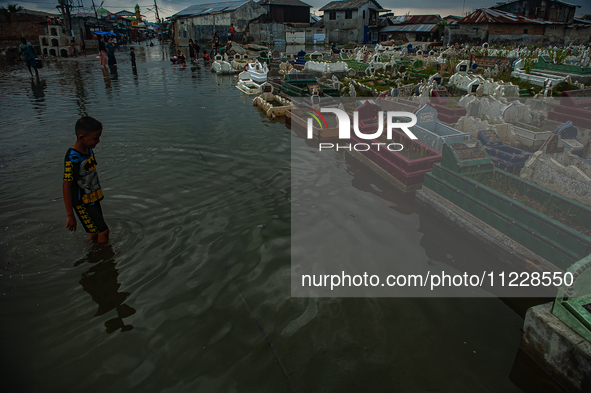 Children are playing at a public cemetery submerged by tidal floods in the Belawan area, Medan, Indonesia, on May 11, 2024. 