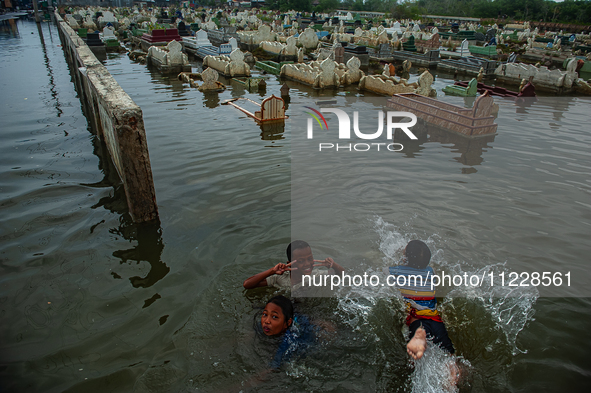 Children are playing at a public cemetery submerged by tidal floods in the Belawan area, Medan, Indonesia, on May 11, 2024. 