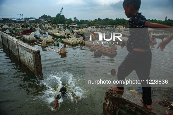 Children are playing at a public cemetery submerged by tidal floods in the Belawan area, Medan, Indonesia, on May 11, 2024. 