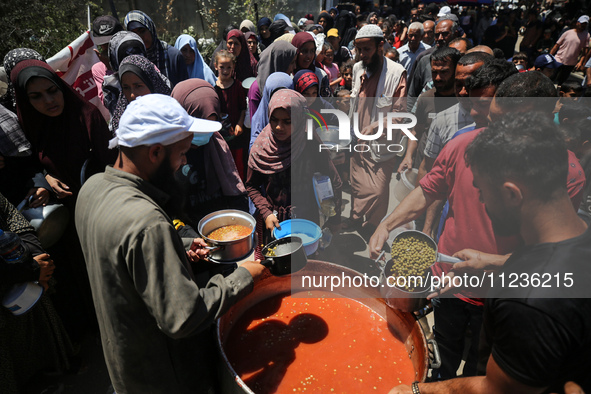 Displaced Palestinians are receiving food portions from a large pot at a public kitchen in Deir el-Balah in the central Gaza Strip on May 13...