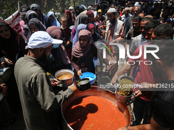 Displaced Palestinians are receiving food portions from a large pot at a public kitchen in Deir el-Balah in the central Gaza Strip on May 13...