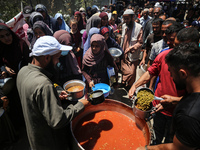 Displaced Palestinians are receiving food portions from a large pot at a public kitchen in Deir el-Balah in the central Gaza Strip on May 13...