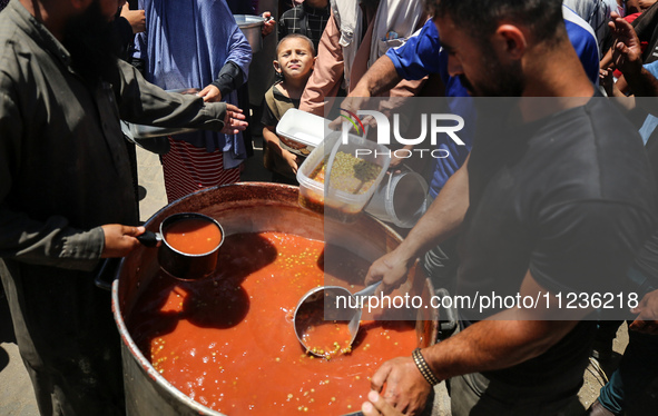 Displaced Palestinians are receiving food portions from a large pot at a public kitchen in Deir el-Balah in the central Gaza Strip on May 13...