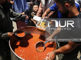 Displaced Palestinians are receiving food portions from a large pot at a public kitchen in Deir el-Balah in the central Gaza Strip on May 13...