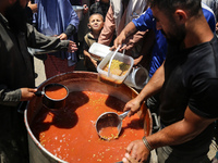 Displaced Palestinians are receiving food portions from a large pot at a public kitchen in Deir el-Balah in the central Gaza Strip on May 13...