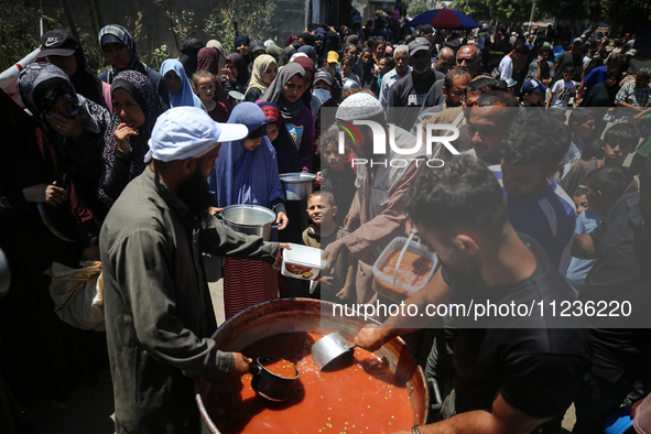 Displaced Palestinians are receiving food portions from a large pot at a public kitchen in Deir el-Balah in the central Gaza Strip on May 13...