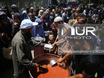 Displaced Palestinians are receiving food portions from a large pot at a public kitchen in Deir el-Balah in the central Gaza Strip on May 13...