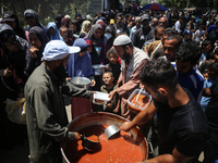 Displaced Palestinians are receiving food portions from a large pot at a public kitchen in Deir el-Balah in the central Gaza Strip on May 13...