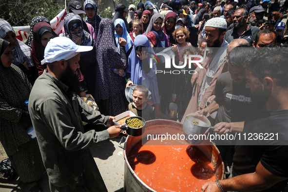 Displaced Palestinians are receiving food portions from a large pot at a public kitchen in Deir el-Balah in the central Gaza Strip on May 13...