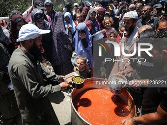 Displaced Palestinians are receiving food portions from a large pot at a public kitchen in Deir el-Balah in the central Gaza Strip on May 13...