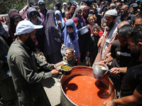 Displaced Palestinians are receiving food portions from a large pot at a public kitchen in Deir el-Balah in the central Gaza Strip on May 13...