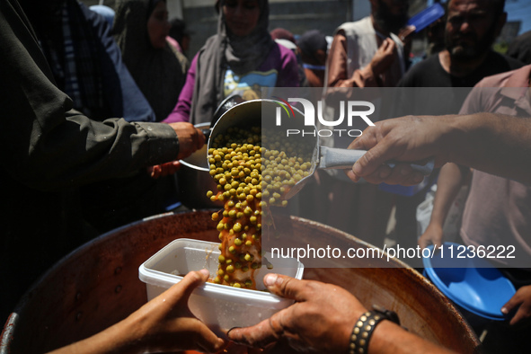 Displaced Palestinians are receiving food portions from a large pot at a public kitchen in Deir el-Balah in the central Gaza Strip on May 13...